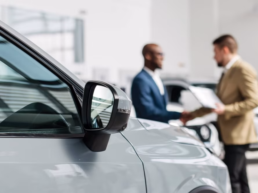 Car salesperson shakes hands with customer in a dealership.