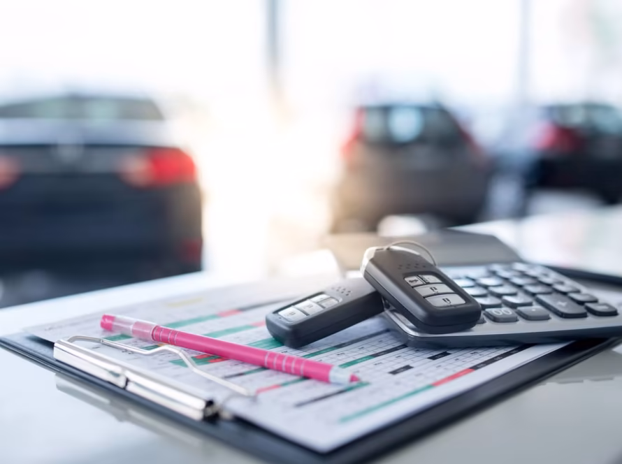 Calculator, pen and car keys on top of paperwork at a car dealership.
