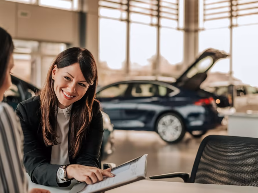 Car saleswoman talking to a customer while pointing to paperwork.