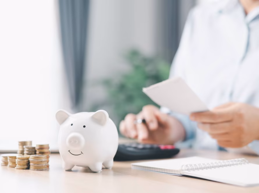 Person calculating costs with a calculator, piggy bank and stack of coins.
