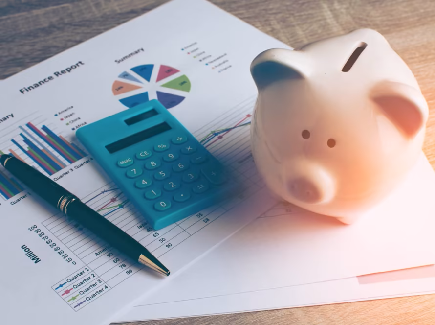 A money piggy bank, calculator and pen placed on top of a finance report document.
